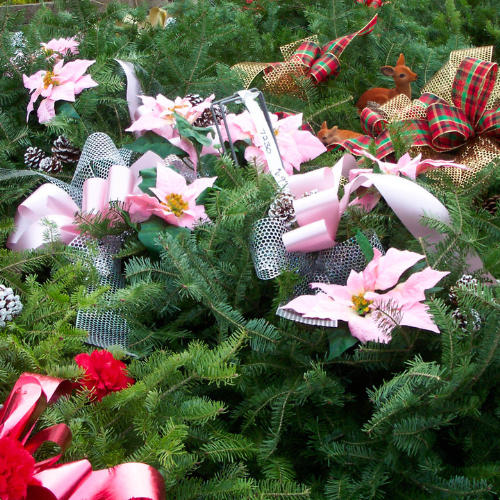 Wreaths decorated with a variety of ribbons in red, pink, and plaid styles. Some feature pink poinsettias, while others are adorned with deer figurines.