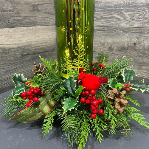 Holiday centerpiece in a Grinch-green vase, featuring an arrangement of pine branches, red berries, ribbon, pinecones, and other festive accents.