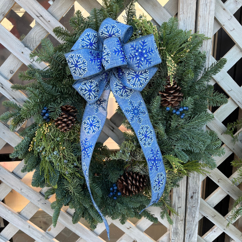 Wreath decorated with a light blue ribbon featuring darker blue snowflakes, accented with pinecones and blue berries around the wreath.