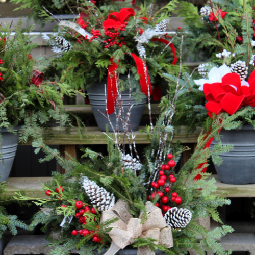 Holiday porch pots in metal containers, decorated with pine branches, pine cones, red bows, and clusters of red berries.