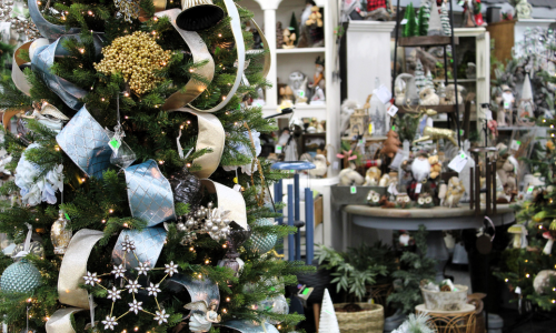 A Christmas tree beautifully decorated with light blue and gold ribbon, silver star-shaped ornaments, gold bells, light blue baubles, and other festive accents.